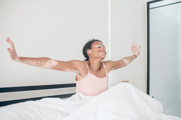 Un Mignon Jeune Mulâtre Assis Dans Son Lit Et L'air Détendu