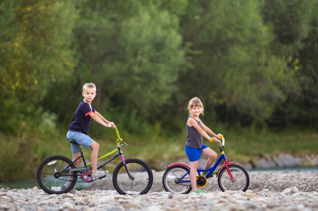 Mignon jeunes enfants blonds, garçon et fille à vélo d'enfant sur la rive de la rivière de galets