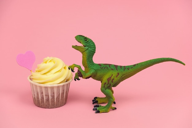 Mignon jouet dinosaure en plastique vert avec cupkace décoré de coeur rose sur fond rose pastel