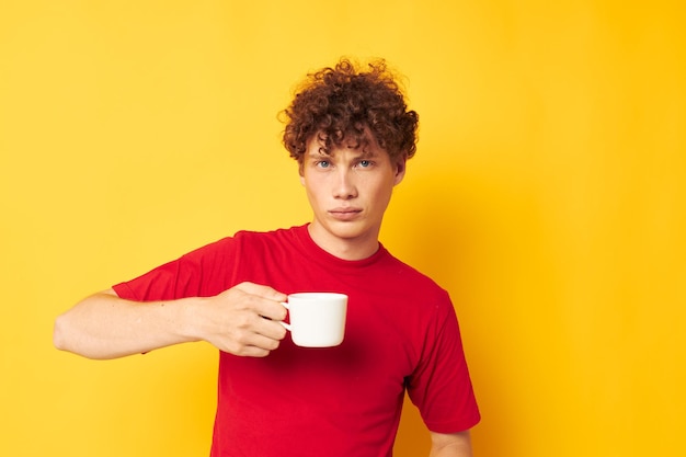 Mignon mec roux posant avec une tasse blanche et dans les mains d'une boisson fond jaune inchangé