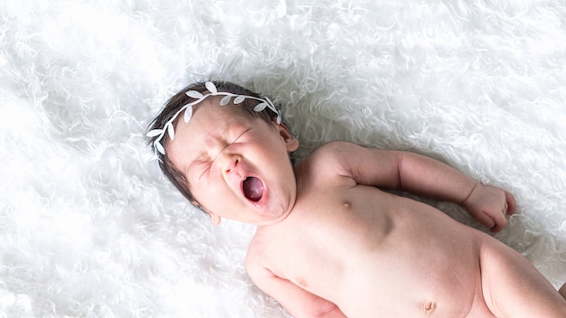 Mignon nouveau-né bâillant sur une fourrure blanche duveteuse