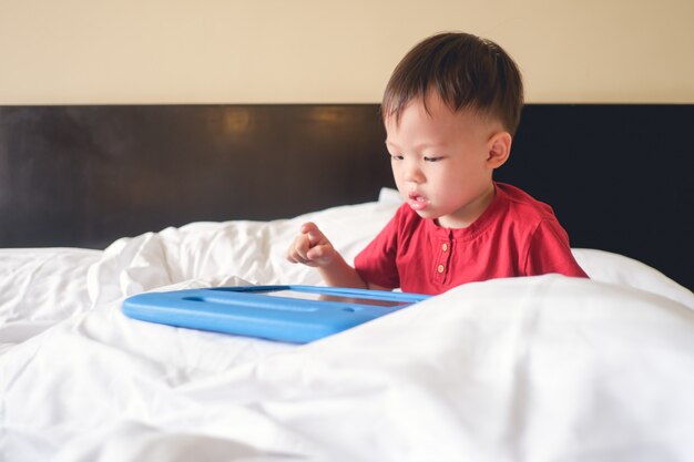 Mignon petit asiatique de 2 à 3 ans enfant garçon enfant assis dans son lit en regardant une vidéo à partir de tablet pc.