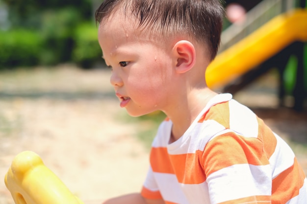 Mignon petit asiatique 2 - 3 ans enfant garçon enfant transpirer pendant qu'il s'amuse à jouer, exercer en plein air au terrain de jeux, concept de coup de chaleur