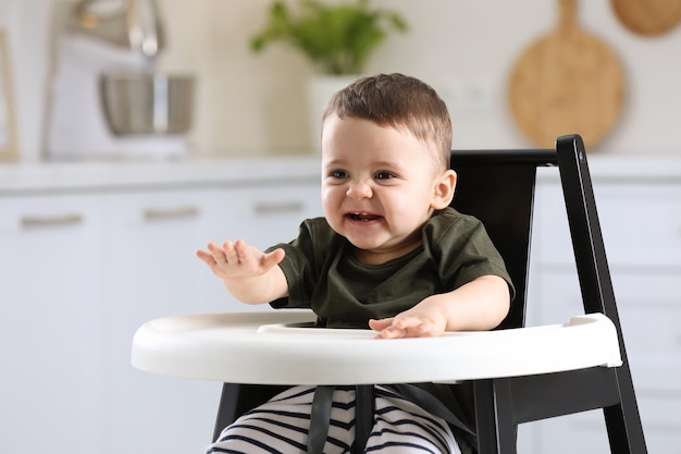 Mignon petit bébé assis dans une chaise haute à la cuisine