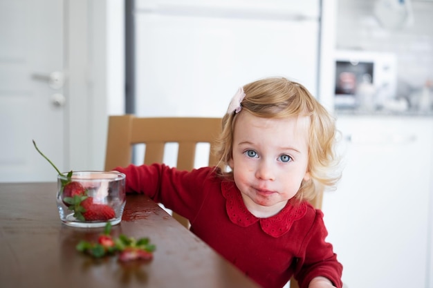 Mignon petit bébé blond caucasien girltoddler adorable bébé mangeant des fraises à partir de la table dans la cuisine