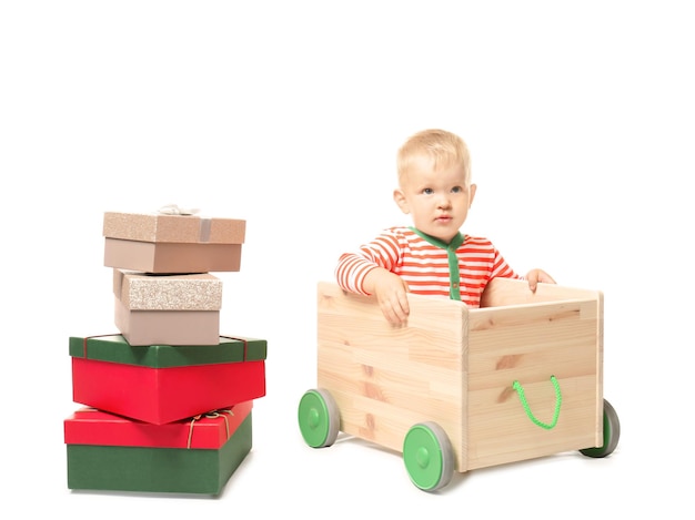 Mignon petit bébé avec chariot de jouets et coffrets cadeaux sur fond blanc. Notion de Noël