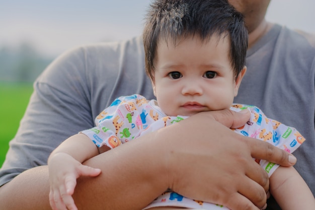 Photo mignon petit bébé dans les bras du père, le père tient la petite fille dans ses mains et sourit aux beaux jours.