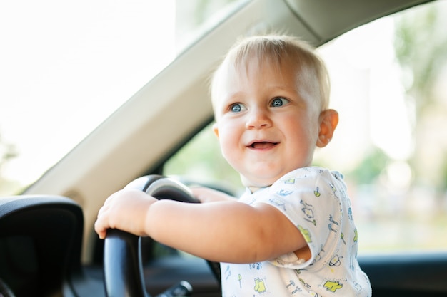 Mignon petit bébé garçon conduisant une grosse voiture, tenant le volant, souriant et impatient avec intérêt.