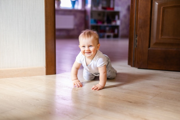 Mignon petit bébé garçon couché sur du bois dur et souriant. Enfant rampant sur un parquet en bois.