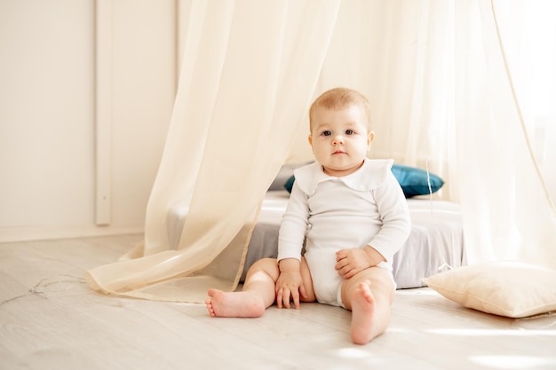 Mignon petit bébé garçon ou fille dans une chambre d'enfant lumineuse avec un wigwam dans un body en coton blanc