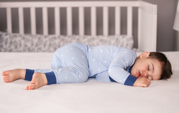 Mignon petit bébé garçon en pyjama bleu clair dormant paisiblement sur le lit à la maison.