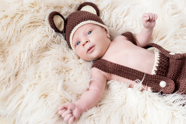 Mignon petit bébé heureux se trouve dans un costume d'ours sur un blanc. nouveau-né dans un chapeau avec des oreilles sur un blanc