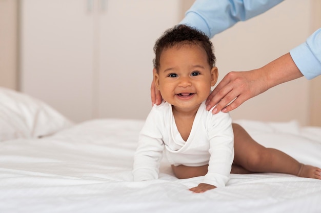 Mignon petit bébé noir relaxant sur le lit pendant que sa mère fait un massage