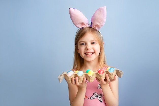 Mignon petit bébé porte des oreilles de lapin le jour de Pâques. jolie petite fille tenant un paquet d'oeufs peints de Pâques