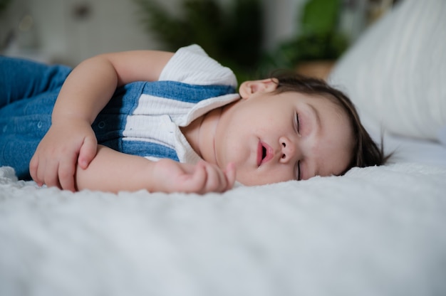 Mignon petit bébé se reposant et dormant confortablement à la maison sur un lit blanc