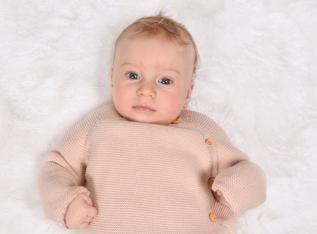 Mignon petit bébé sérieux caucasien, regardant la caméra, allongé sur le dos sur blanc.