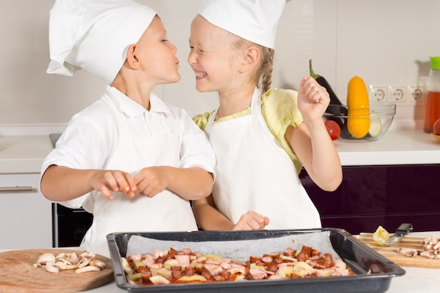 Mignon petit chef embrassant sa soeur chef dans la cuisine. Enfants très heureux.