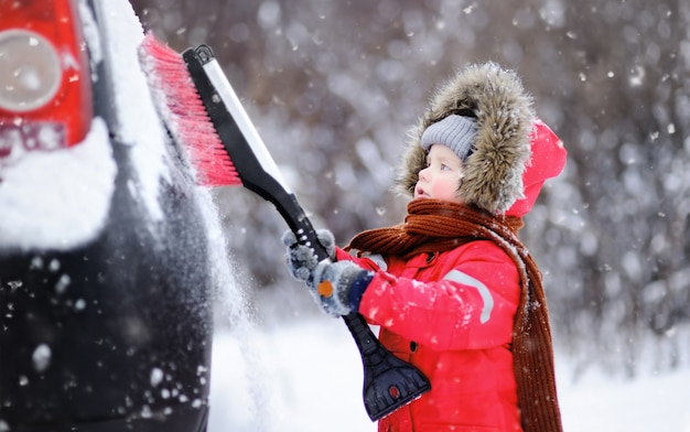 Mignon petit enfant aidant à brosser la neige d&#39;une voiture