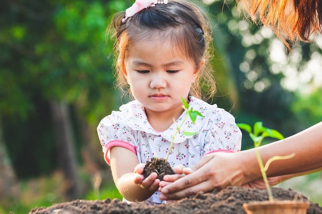 Mignon petit enfant asiatique fille et parent planter ensemble de jeunes plants dans le sol noir