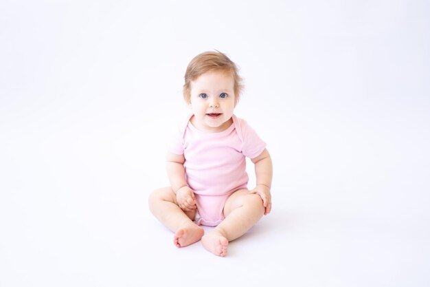 Un mignon petit enfant en bonne santé dans un body rose est assis et sourit sur un fond blanc une place pour le texte