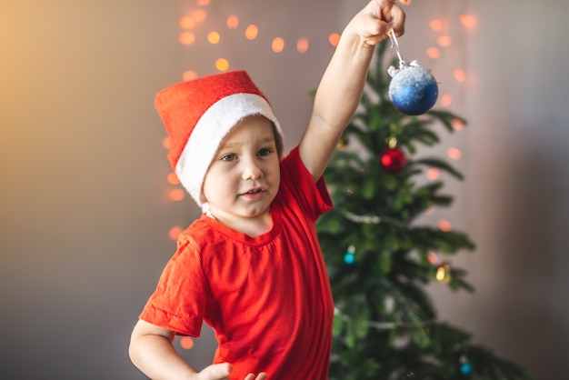 Mignon petit enfant dans un bonnet de Noel tient une boule de Noël