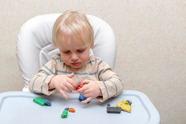 Mignon petit enfant garçon jouant à la maison en train de mouler de la pâte à modeler multicoloreLes mains des enfants sculptent avec du stuc d'argile colorée