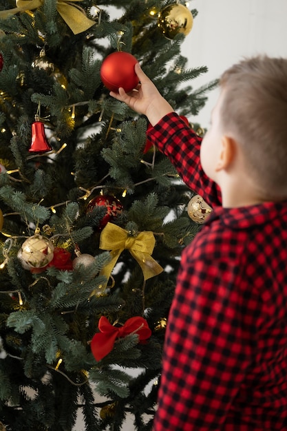 mignon petit enfant garçon en pyjama rouge décoré d'arbre de noël à la maison