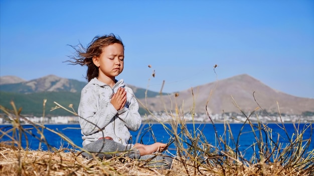 Photo mignon petit enfant gurl méditant seul en posture de lotus au bord du lac