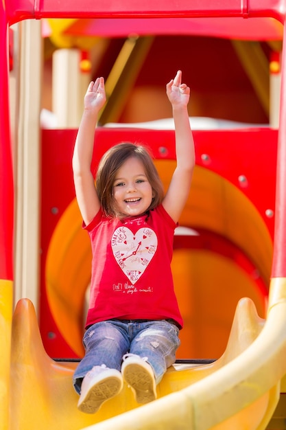 Un mignon petit garçon de 3 ans joue avec enthousiasme sur un toboggan jaune pour aire de jeux par une fraîche journée nuageuse