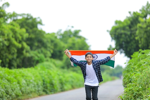 Mignon petit garçon en agitant le drapeau tricolore national indien sur fond de nature