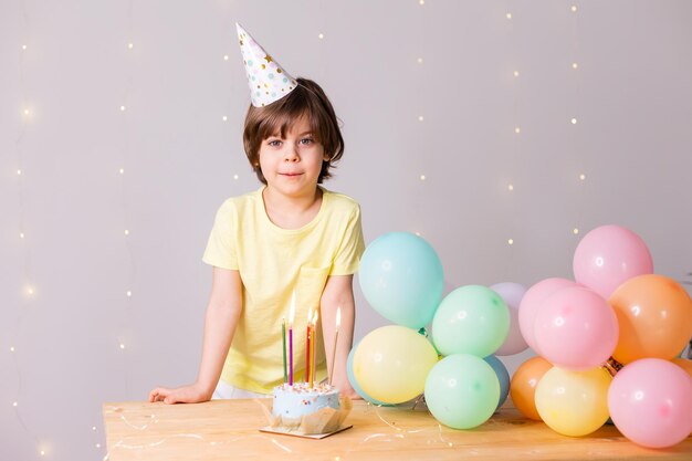 Mignon petit garçon d'anniversaire dans un gâteau au chapeau avec des bougies ballons joyeux anniversaire