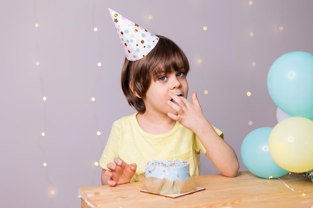 mignon petit garçon d'anniversaire mangeant un gâteau dans des ballons de chapeau joyeux anniversaire