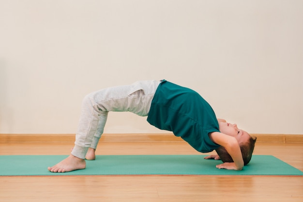 Un mignon petit garçon apprend à faire du yoga dans la salle de sport