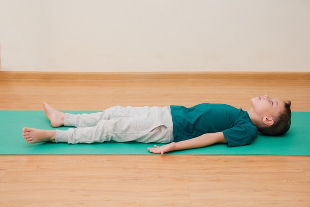 Un mignon petit garçon apprend à faire du yoga dans la salle de sport