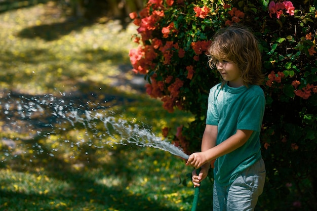 Mignon petit garçon arrosant des fleurs dans le jardin le jour d'été Enfant à l'aide d'un tuyau d'arrosage Eau drôle pour enfant