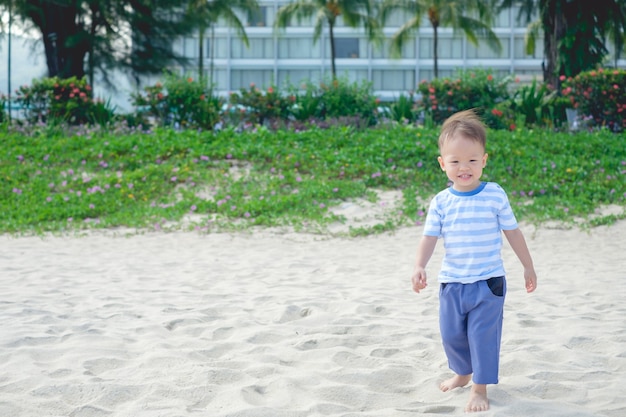 mignon petit garçon asiatique souriant heureux debout pieds nus sur une plage tropicale de sable