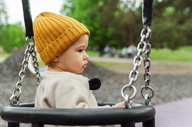 Mignon petit garçon assis sur une balançoire dans un parc public