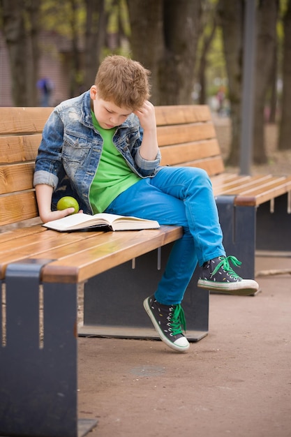 Mignon petit garçon assis sur un banc dans le parc et lisant un livre Enfant apprenant et lisant à l'extérieur Écolier avec un livre à l'extérieur