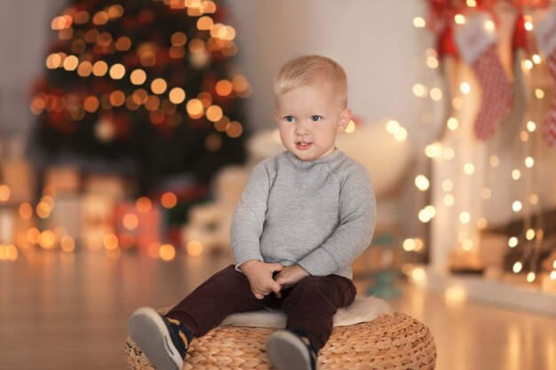 Mignon petit garçon assis sur une chaise ottomane décorée pour la salle de Noël