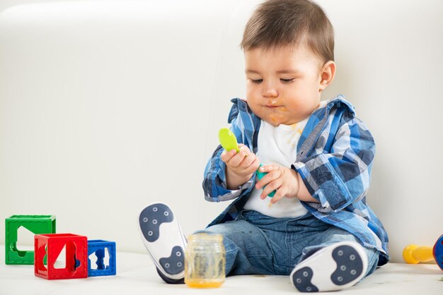 Mignon petit garçon assis à la maison et jouant avec une cuillère