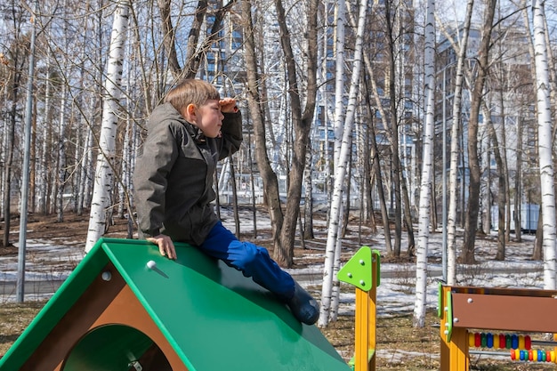 Mignon petit garçon athlétique de 67 ans jouant dans une aire de jeux Parc d'attractions pour enfants Activités de plein air et jeux pour enfants Un enfant joyeux est assis haut sur une maison de jouets en bois