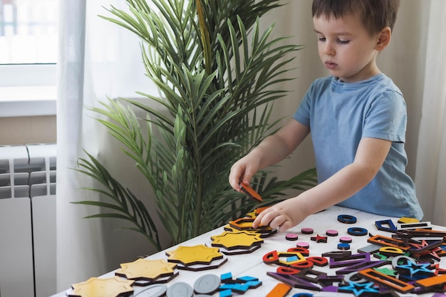 Mignon petit garçon attentif apprenant des formes de figures géométriques jouant à la construction en bois multicolore