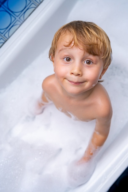 Mignon petit garçon blond jouant et prenant un bain dans la baignoire