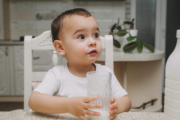 Mignon petit garçon boit du lait à la table dans le mocap de bouteille de lait de cuisine