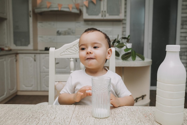 Mignon petit garçon boit du lait à la table dans le mocap de bouteille de lait de cuisine