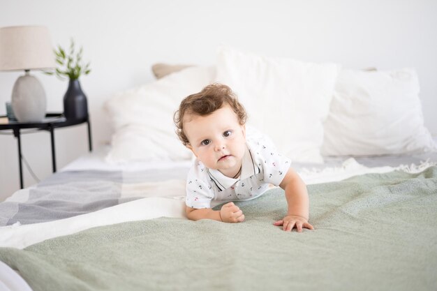 Mignon petit garçon en bonne santé dans une chambre spacieuse et lumineuse est assis sur un lit sur du linge de lit blanc l'enfant sourit des textiles pour la chambre et la crèche