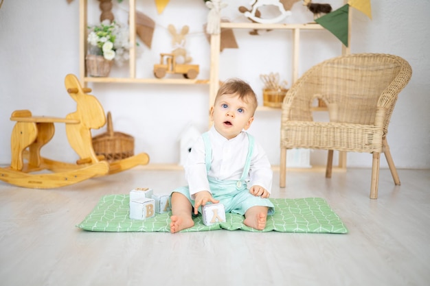Un mignon petit garçon en bonne santé joue avec des jouets éducatifs en bois dans une chambre d'enfants confortable et lumineuse à la maison sur le fond d'une maison en bois