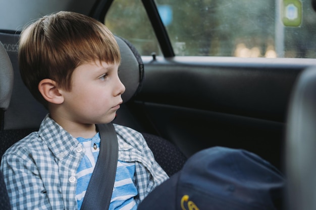 Mignon petit garçon caucasien assis dans un siège enfant voyageant en voiture fatigué et ennuyé