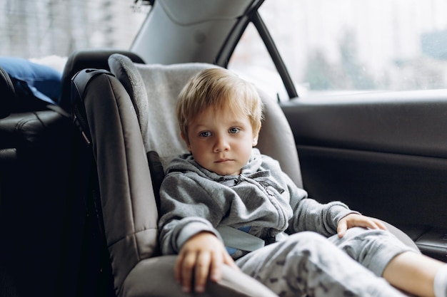 Mignon petit garçon caucasien au visage triste assis dans un siège de sécurité pour enfant dans une voiture