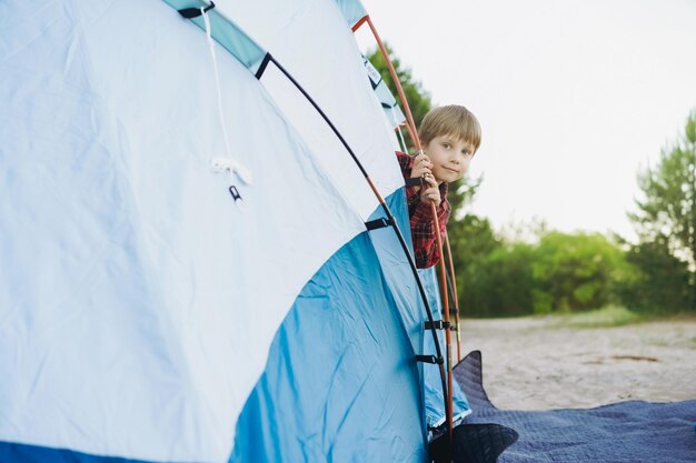 Un mignon petit garçon caucasien regardant depuis une tente touristique Concept de camping familial